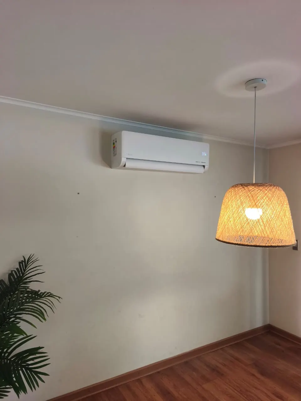 Equipo split instalado en la pared de un dormitorio, junto a una lámpara de mimbre.