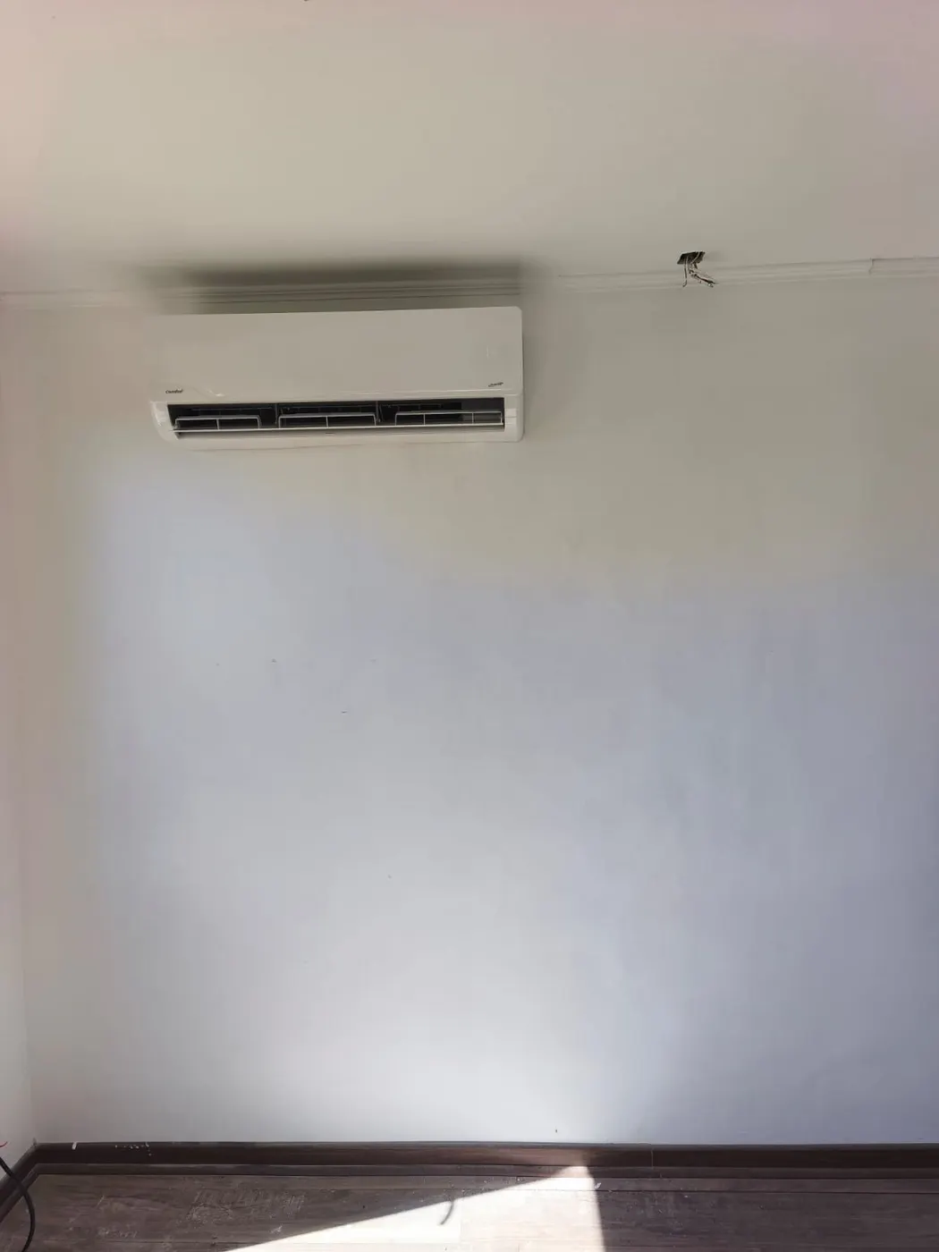 Equipo split blanco recién instalado en la pared de una habitación, con la canaleta corriendo hasta el pasamuros.