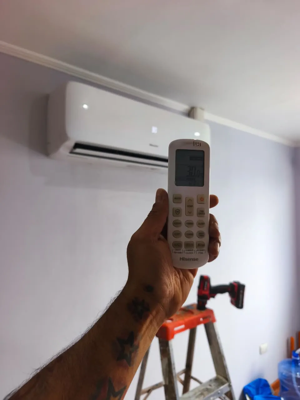 Mano sosteniendo el control remoto de un equipo Hisense en 30 grados, frente al split encendido.